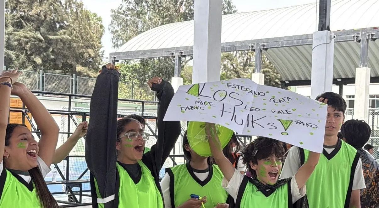 Alumnos con petos verdes animan con un cartel hecho a mano durante una jornada escolar